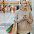 Junge Frau mit weißen Kopfhörern und Einkaufstaschen schlendert durch ein helles Einkaufszentrum