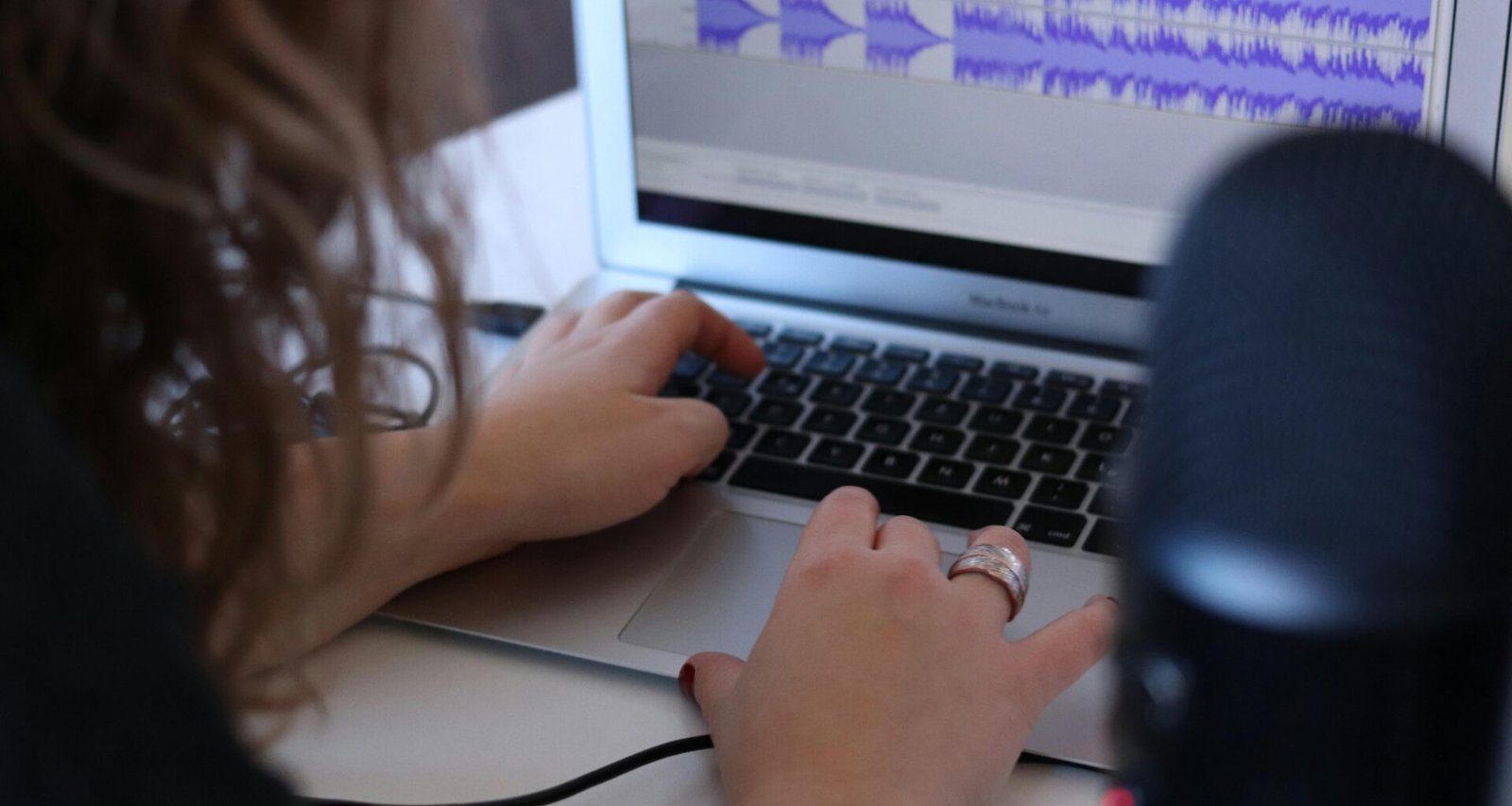 Frau sitzt mit einem MacBook Air an einem Tisch in einem hellen Raum und arbeitet konzentriert am Laptop.