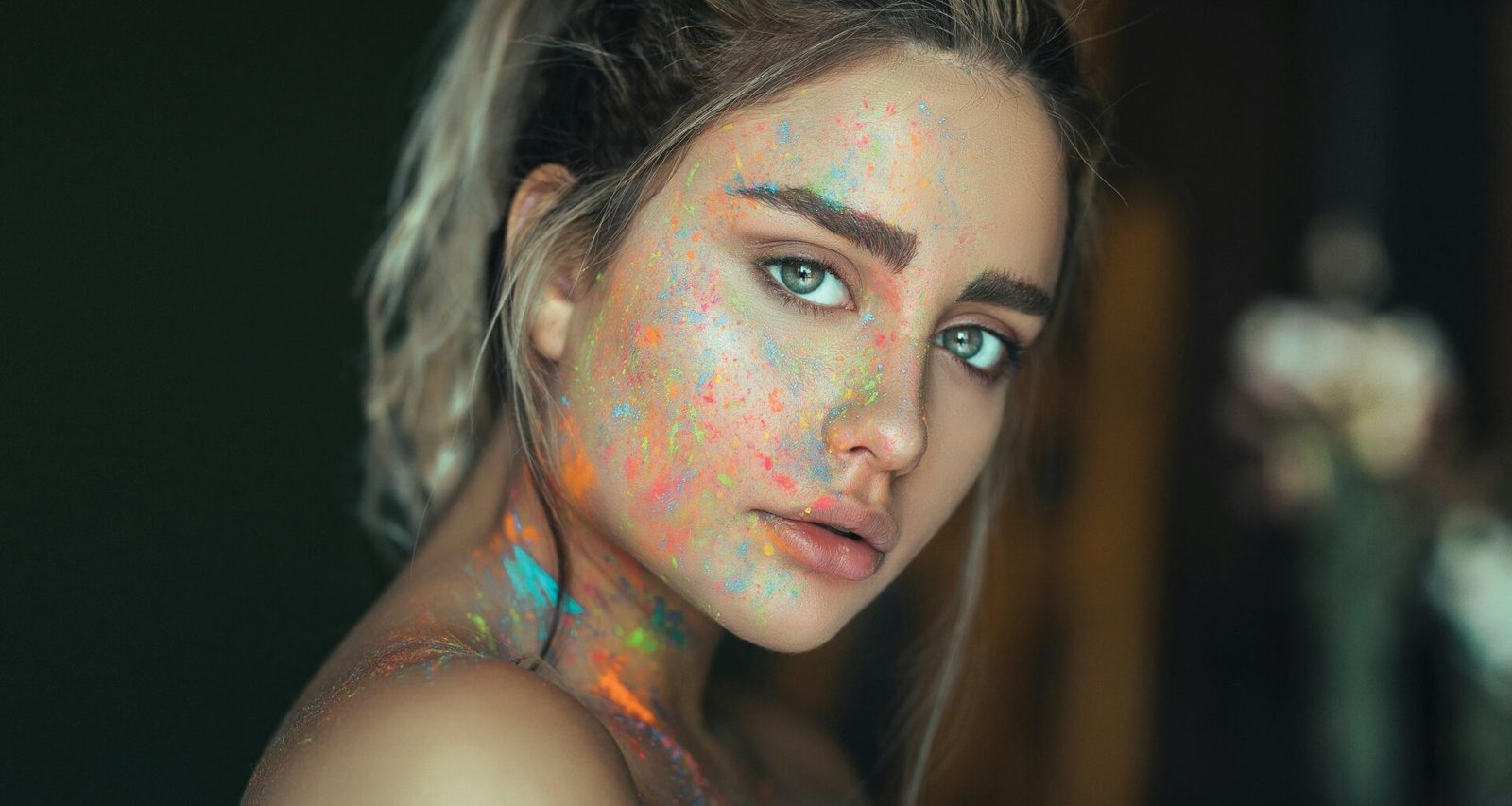 Frau mit auffälliger, mehrfarbiger Gesichtsbemalung vor neutralem Hintergrund, moderner künstlerischer Ausdruck