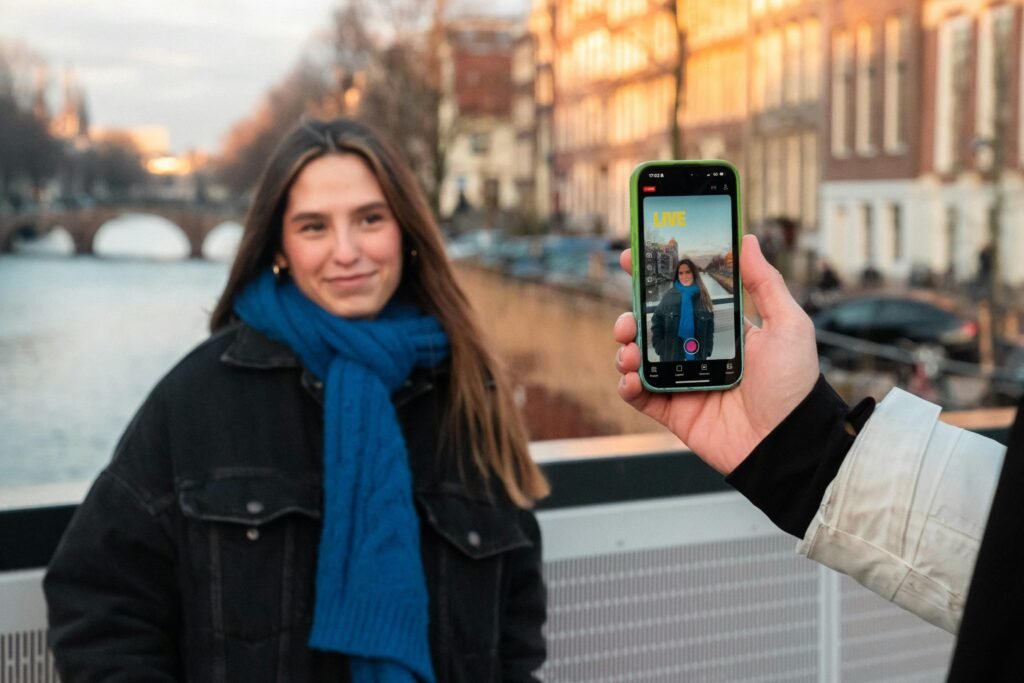 Junge Frau fotografiert sich selbst mit dem Smartphone vor einem ruhigen Kanal in einer Stadt