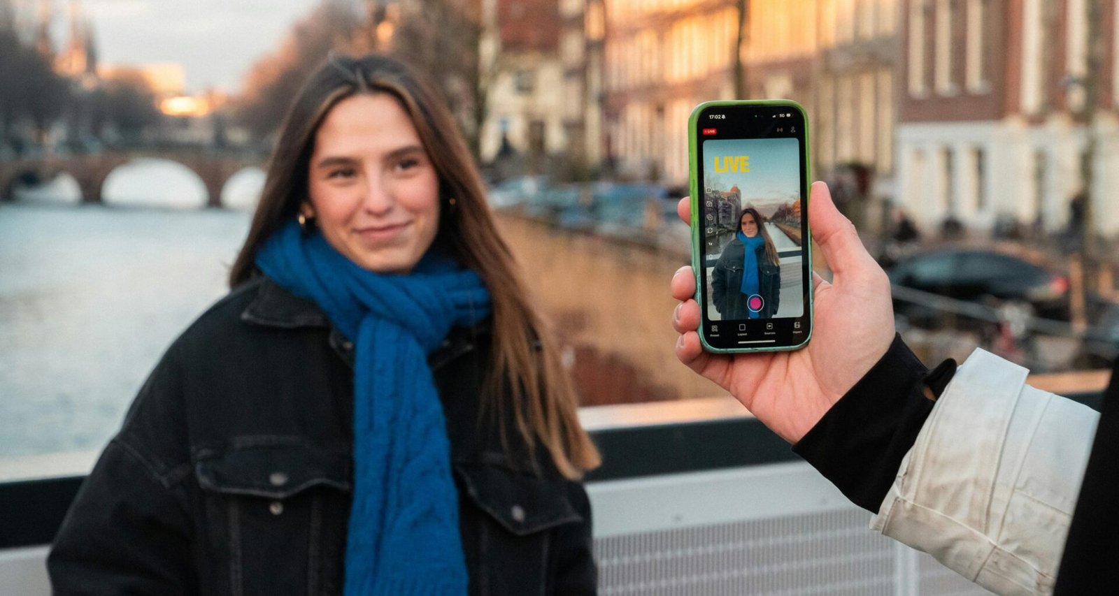 Junge Frau fotografiert sich selbst mit dem Smartphone vor einem ruhigen Kanal in einer Stadt