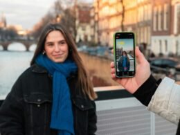 Junge Frau fotografiert sich selbst mit dem Smartphone vor einem ruhigen Kanal in einer Stadt