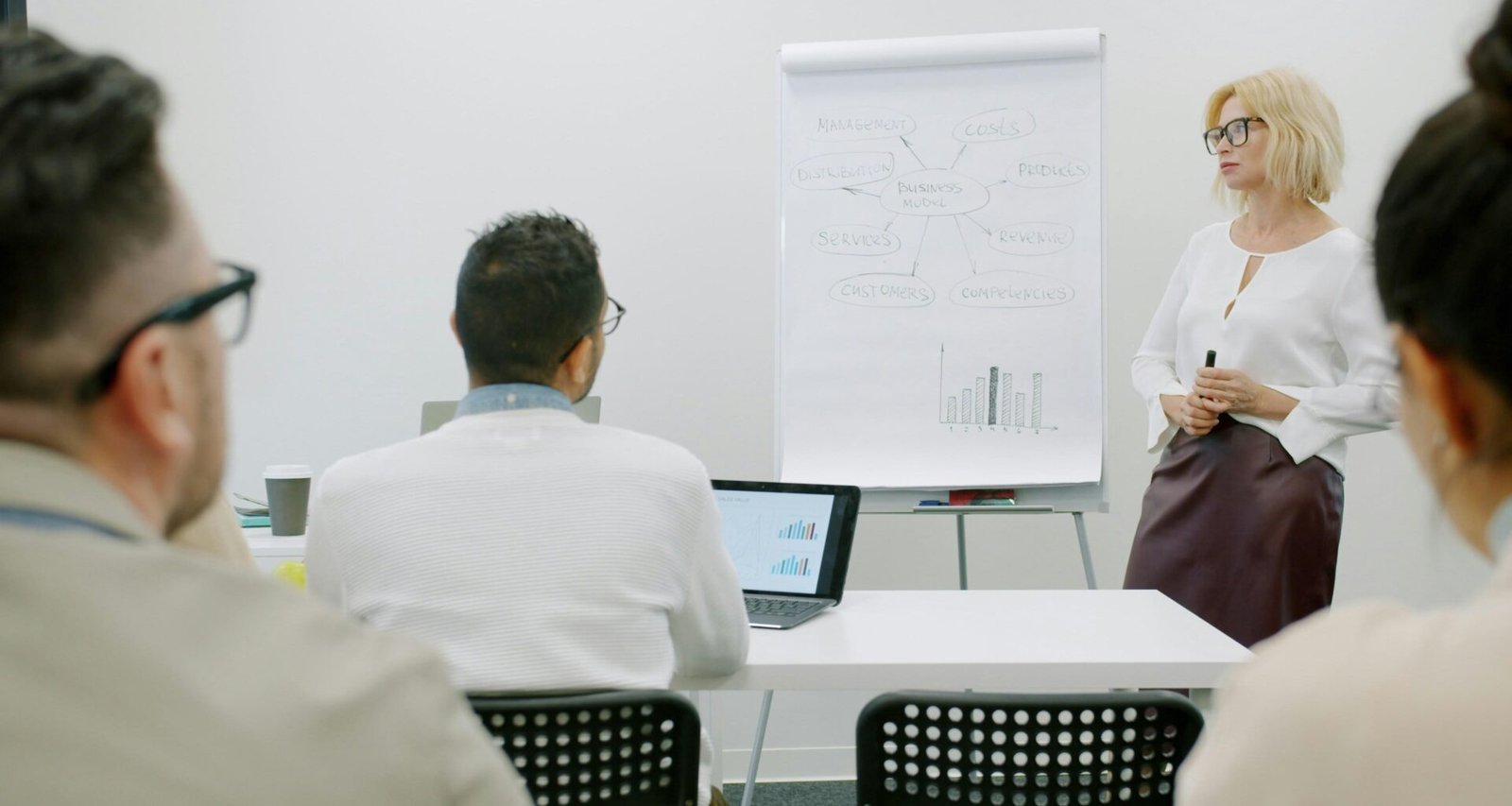 Frau präsentiert vor Zuhörern in einem modernen Büro, Fokus auf professionelle Team-Kommunikation im Arbeitsumfeld