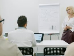Frau präsentiert vor Zuhörern in einem modernen Büro, Fokus auf professionelle Team-Kommunikation im Arbeitsumfeld