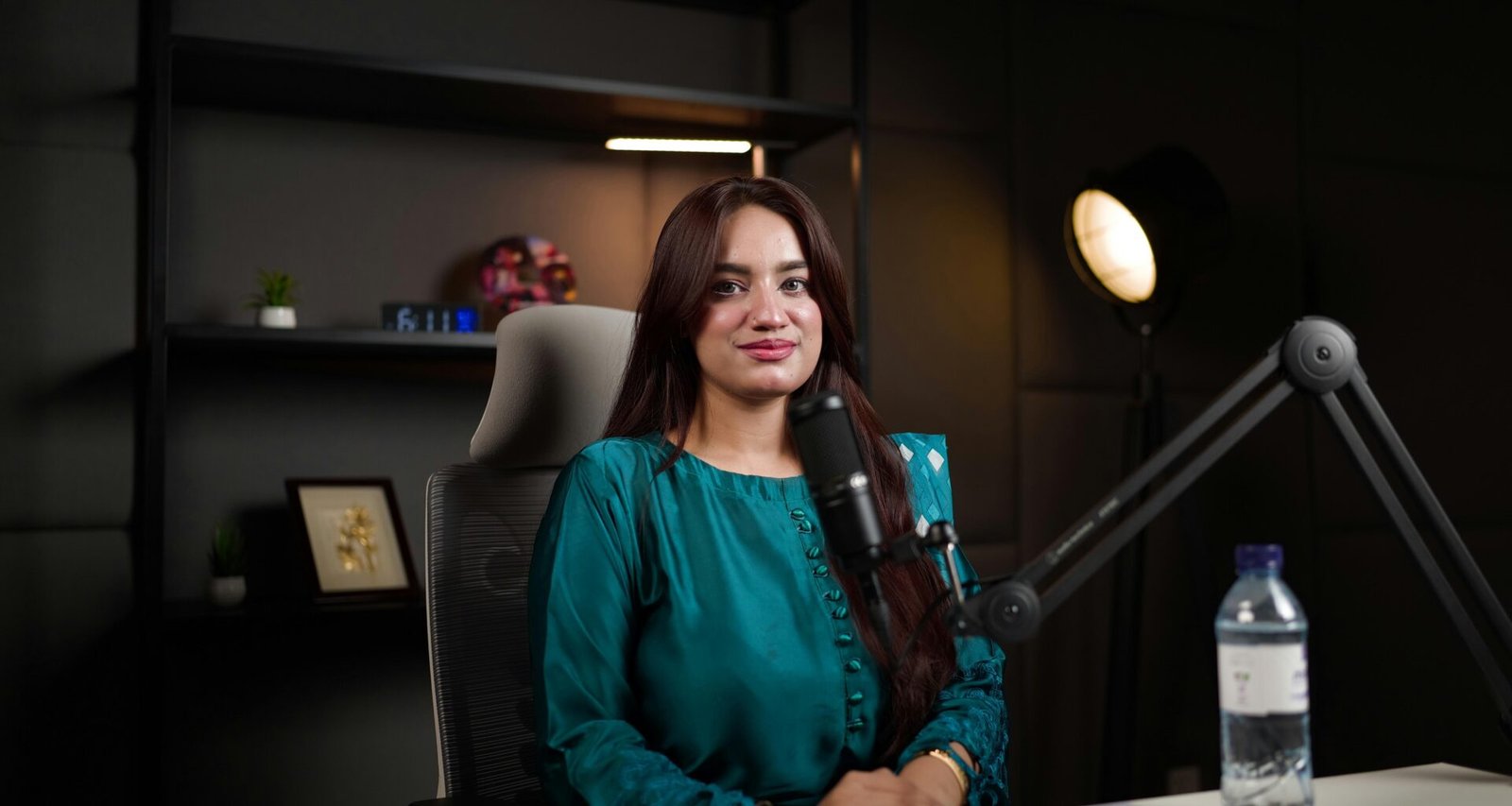 Frau an einem Schreibtisch mit Mikrofon und Wasserflasche – Aufnahme einer modernen Podcast-Szene im Büro