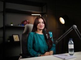 Frau an einem Schreibtisch mit Mikrofon und Wasserflasche – Aufnahme einer modernen Podcast-Szene im Büro