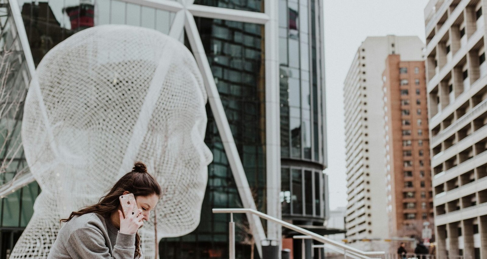Frau sitzt draußen auf dem Boden vor einem Gebäude und hält ihr Smartphone in der Hand – moderne mobile Nutzung