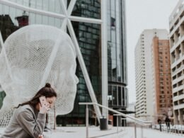 Frau sitzt draußen auf dem Boden vor einem Gebäude und hält ihr Smartphone in der Hand – moderne mobile Nutzung
