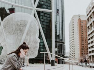 Frau sitzt draußen auf dem Boden vor einem Gebäude und hält ihr Smartphone in der Hand – moderne mobile Nutzung