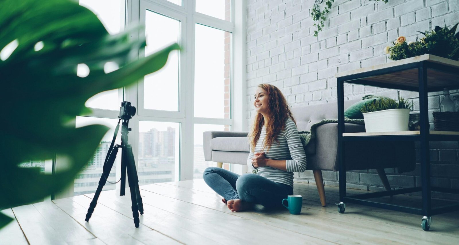 Eine Frau sitzt auf dem Boden vor einer Kamera und nimmt Videoaufnahmen in ihrem Wohnraum auf.