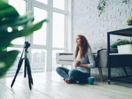 Eine Frau sitzt auf dem Boden vor einer Kamera und nimmt Videoaufnahmen in ihrem Wohnraum auf.