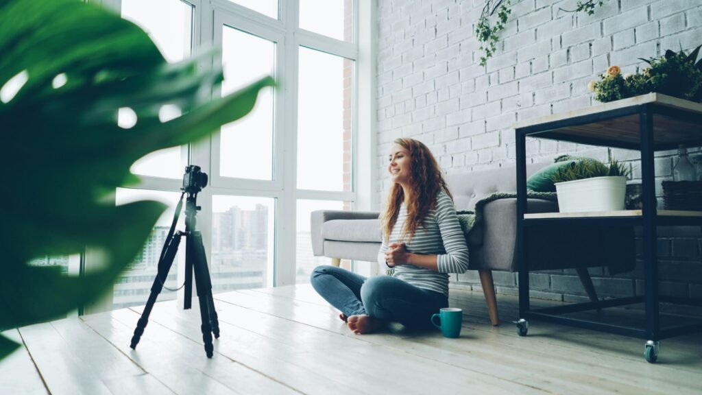 Frau sitzt auf dem Boden und filmt sich selbst mit einer Kamera für einen Videobeitrag