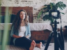 Frau sitzt auf dem Boden und nimmt sich mit einer Kamera beim Videoaufnehmen in einem Innenraum auf.