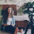 Eine Frau sitzt auf dem Boden in einem modernen Raum und nimmt mit einer Kamera vor sich ein Video auf.