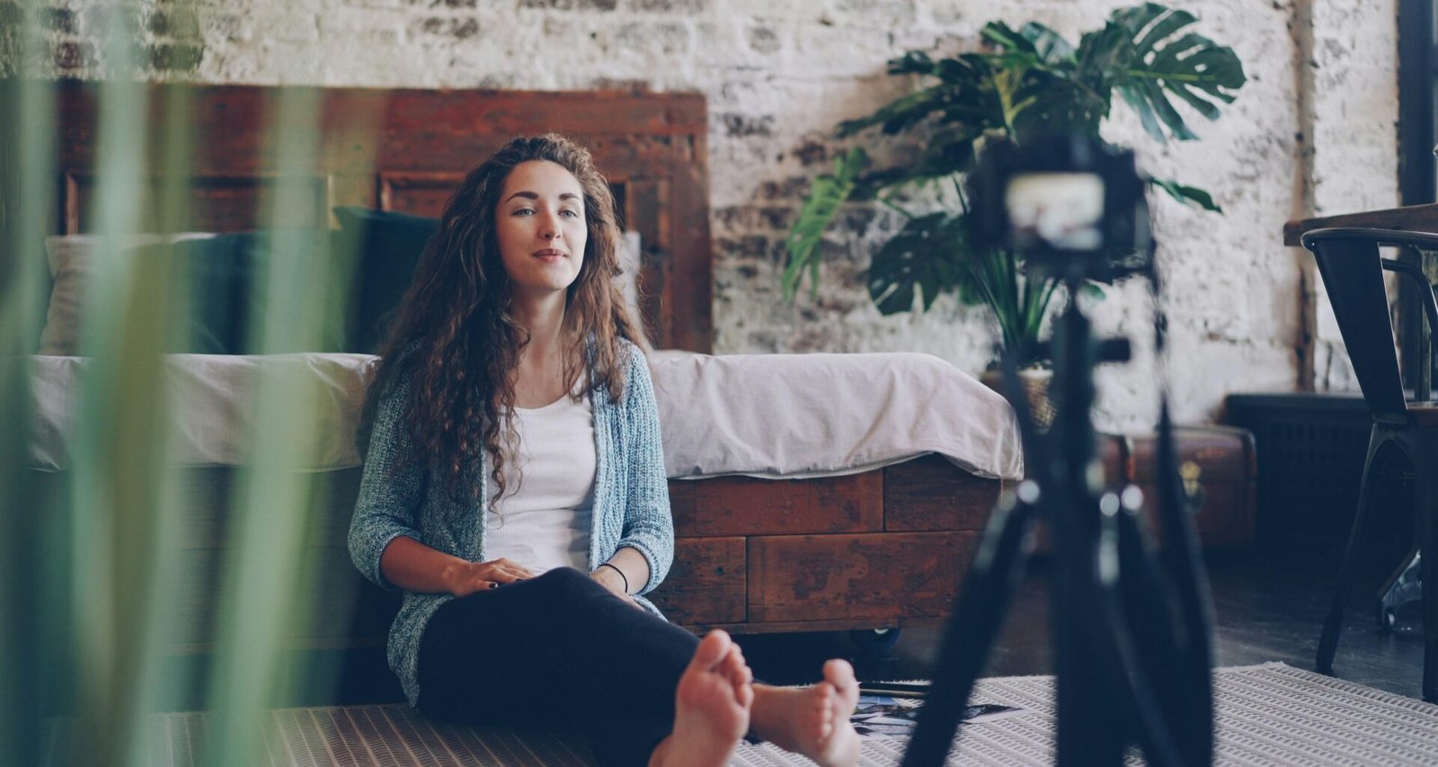 Eine Frau sitzt auf dem Boden in einem modernen Raum und nimmt mit einer Kamera vor sich ein Video auf.