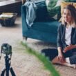 Frau sitzt auf dem Fußboden und filmt sich selbst mit einer Kamera für Social-Media-Beiträge