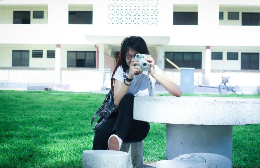 Frau sitzt auf einem weißen Betonstuhl und fotografiert mit ihrem Smartphone im Außenbereich