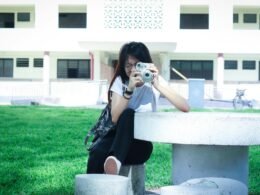 Frau sitzt auf einem weißen Betonstuhl und fotografiert mit ihrem Smartphone im Außenbereich