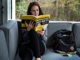 Frau sitzt auf einem Sofa, liest ein Buch und hat eine Tasche neben sich, fokussiert auf entspannte Leseatmosphäre im Wohnzimmer