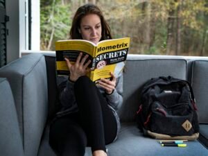 Frau sitzt auf einem Sofa, liest ein Buch und hat eine Tasche neben sich, fokussiert auf entspannte Leseatmosphäre im Wohnzimmer