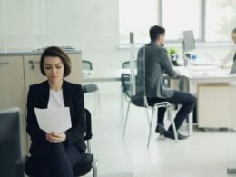 Eine Frau sitzt an einem modernen Büroschreibtisch und hält mehrere Papierdokumente in den Händen