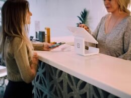 Eine Frau steht neben einem Monitor in einem hellen Büro und betrachtet den Bildschirm aufmerksam