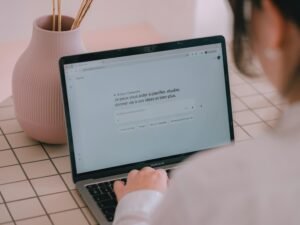 Frau tippt auf einem Laptop an einem Schreibtisch, daneben steht eine Vase mit Blumen im modernen Homeoffice.