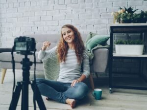 Frau winkt in die Kamera während sie ein Video in ihrem Wohnzimmer aufnimmt, Fokus auf Heimaufnahme und Content-Erstellung.