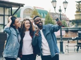 Gruppe von Freunden, die gemeinsam auf einer belebten Straße in einer Stadt ein Selfie aufnehmen