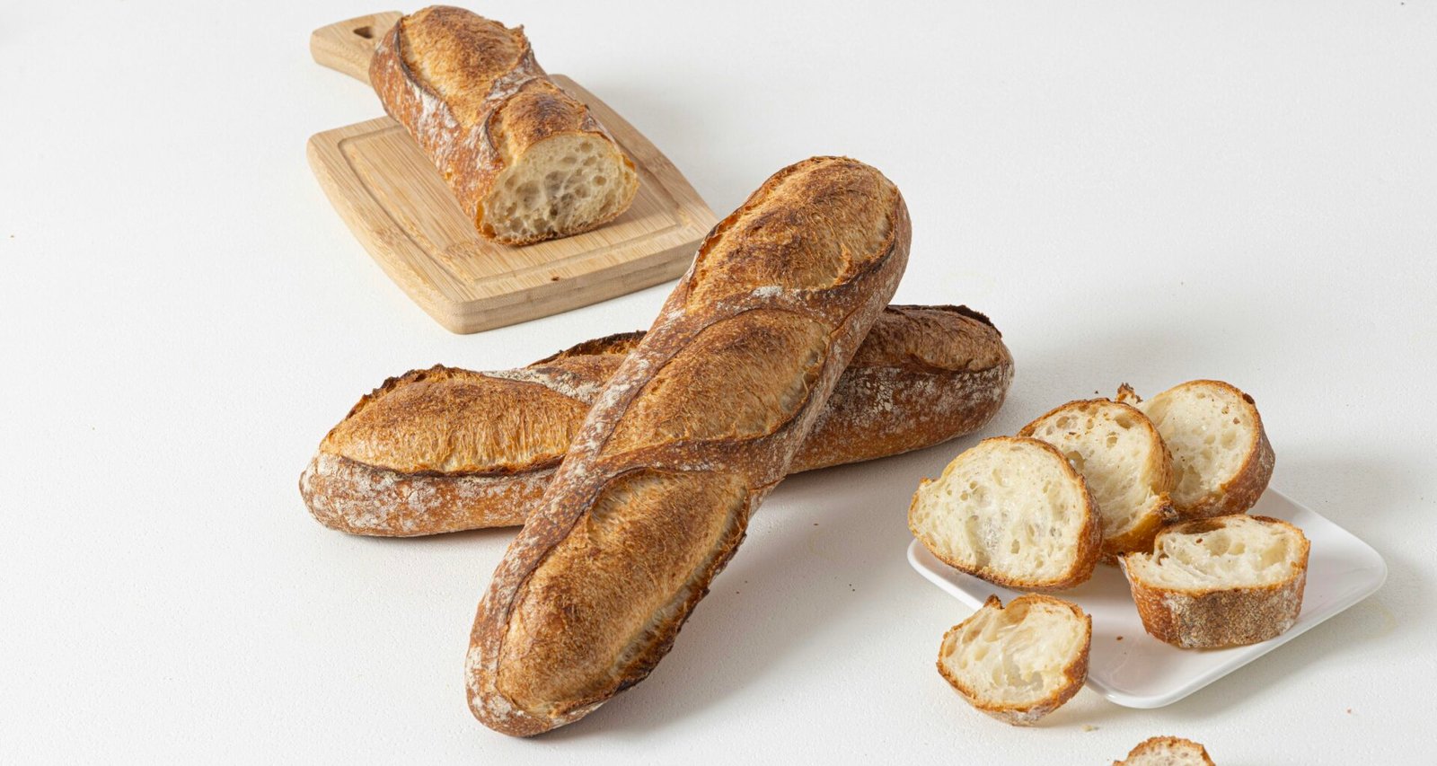 Frisch gebackene Baguettes und mehrere Brotscheiben auf einer weißen Oberfläche, fotografiert aus der Vogelperspektive