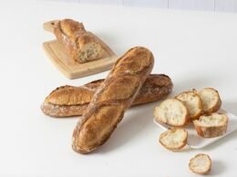 Frisch gebackene Baguettes und mehrere Brotscheiben auf einer weißen Oberfläche, fotografiert aus der Vogelperspektive