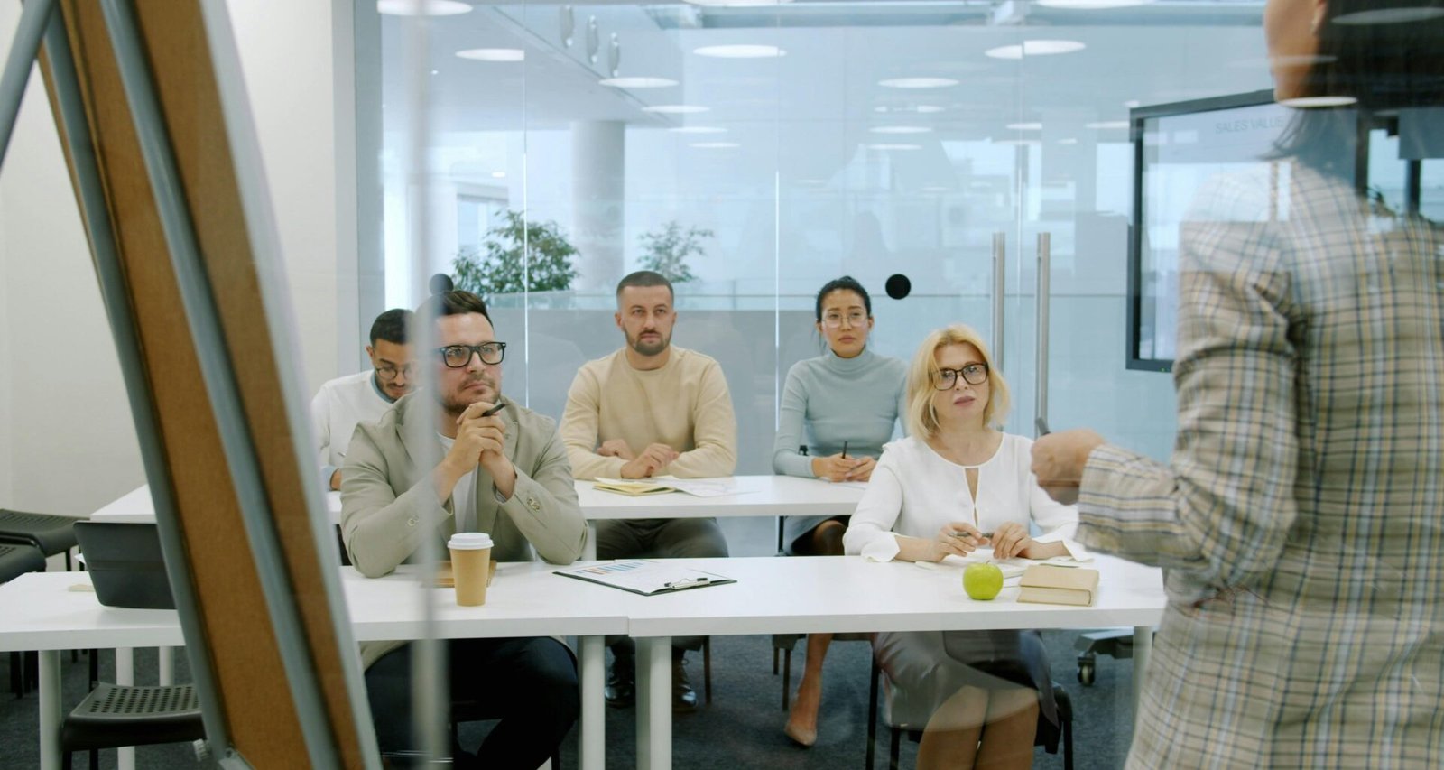 Mehrere Geschäftsleute sitzen in einem modernen Büro und nehmen aufmerksam an einer Präsentation mit Bildschirmen teil.