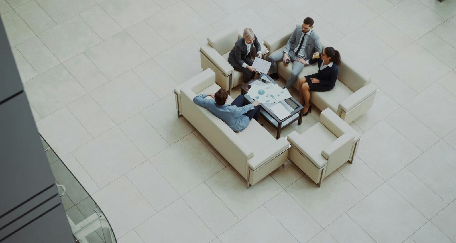 Mehrere Geschäftsleute sitzen auf Sofas in einer hellen, modernen Hotellobby und führen ein Meeting durch.