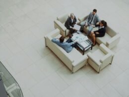 Mehrere Geschäftsleute sitzen auf Sofas in einer hellen, modernen Hotellobby und führen ein Meeting durch.
