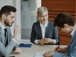 Zwei Geschäftsleute sitzen an einem Tisch und unterzeichnen gemeinsam einen Vertrag mit Kugelschreibern.