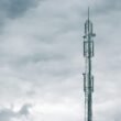 Grauer Radio- oder Funkturm steht bei Tageslicht unter einer dichten Wolkendecke am Himmel
