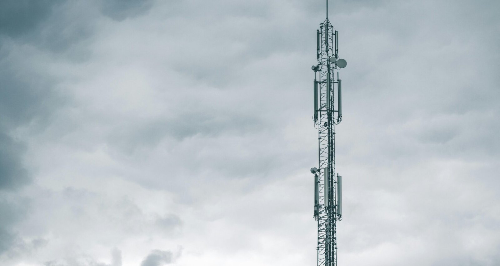 Grauer Radio- oder Funkturm steht bei Tageslicht unter einer dichten Wolkendecke am Himmel