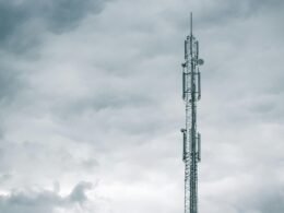 Grauer Radio- oder Funkturm steht bei Tageslicht unter einer dichten Wolkendecke am Himmel