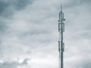 Grauer Radio- oder Funkturm steht bei Tageslicht unter einer dichten Wolkendecke am Himmel