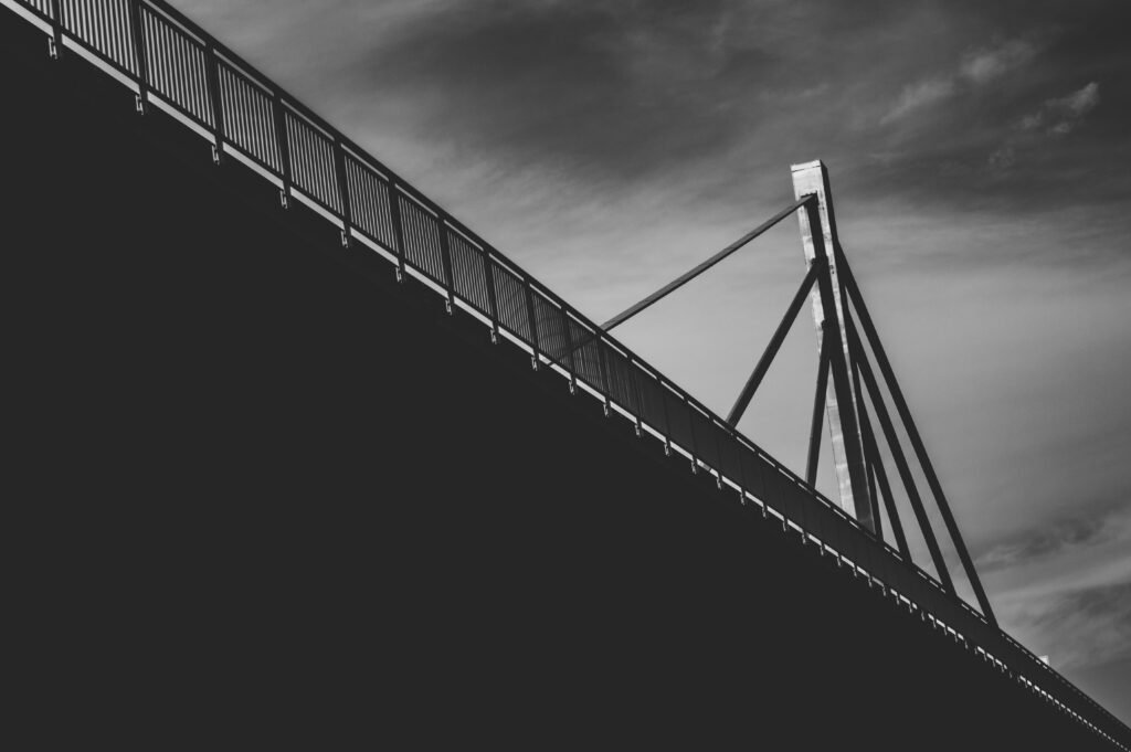 Grayscale-Fotografie einer modernen Kabelbrücke mit markanter Seilstruktur, aufgenommen aus Unteransicht
