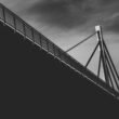 Grayscale-Fotografie einer modernen Kabelbrücke mit markanter Seilstruktur, aufgenommen aus Unteransicht