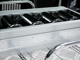 Schwarzweißaufnahme eines rechteckigen grauen Gehäuses auf einem Drahtregal, minimalistische Technik-Darstellung