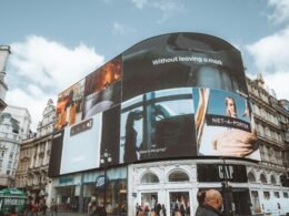 Großes, gebogenes Gebäude mit zahlreichen digitalen Werbetafeln an der Fassade in urbanem Umfeld