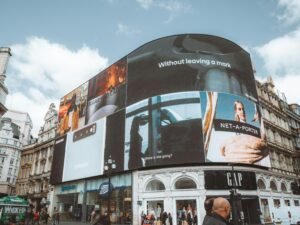Großes, gebogenes Gebäude mit zahlreichen digitalen Werbetafeln an der Fassade in urbanem Umfeld