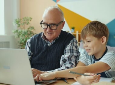Ein älterer Mann und ein Junge sitzen nebeneinander und schauen interessiert zusammen auf einen offenen Laptop.