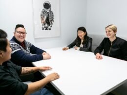 Vier Menschen sitzen um einen weißen Konferenztisch und führen ein gemeinsames Meeting im Büro