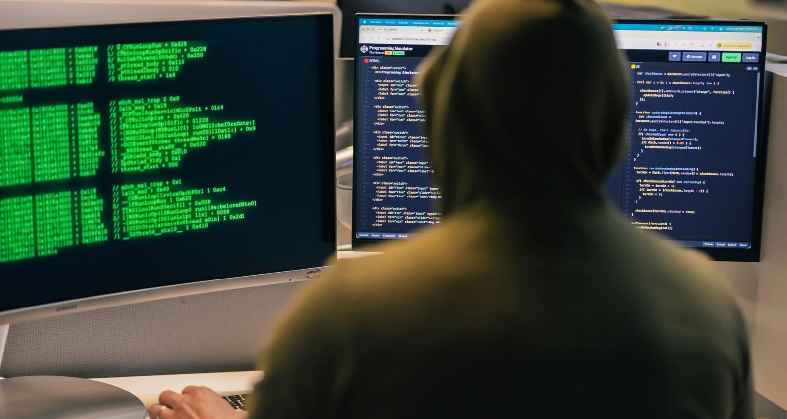 Ein Hacker mit Kapuze sitzt vor mehreren Computerbildschirmen und arbeitet an komplexen digitalen Aufgaben im Büro.