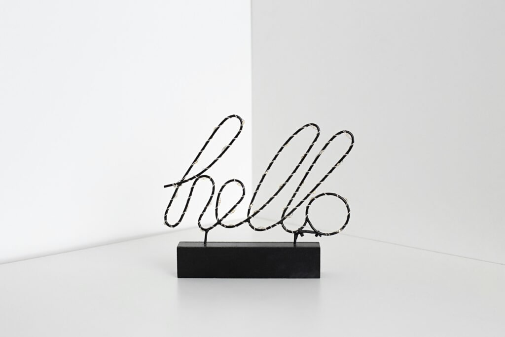 Ein schwarzes Schild mit weißer Aufschrift 'hello' auf hellem Hintergrund, minimalistisch gestaltet