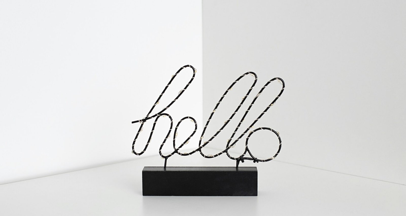 Ein schwarzes Schild mit weißer Aufschrift 'hello' auf hellem Hintergrund, minimalistisch gestaltet