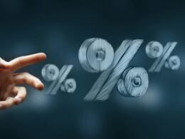 Eine Hand erreicht nach mehreren frei schwebenden Prozentzeichen vor neutralem Hintergrund – Symbolbild für Zinsen oder Rabatte.